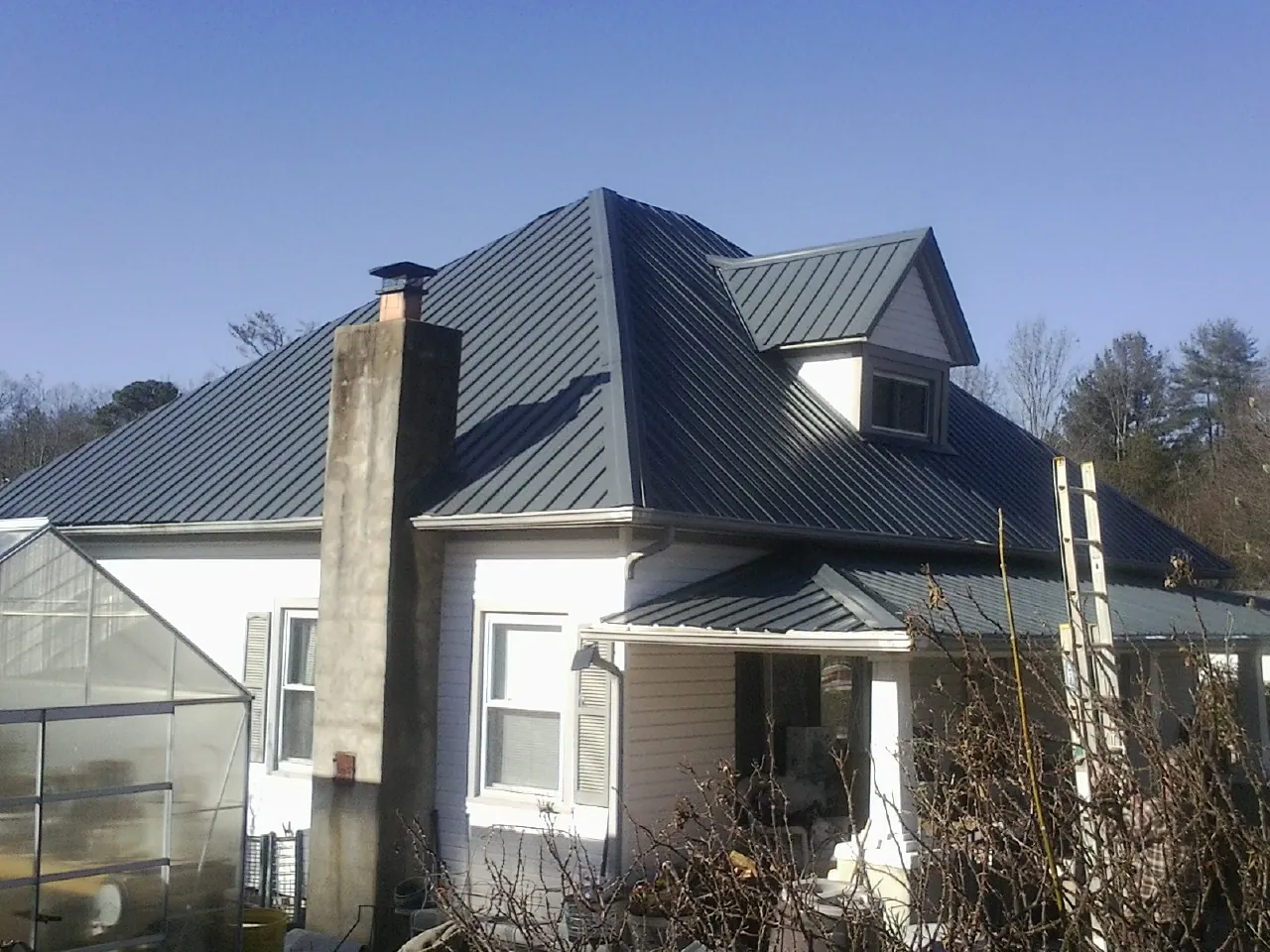 Dark blue standing seam metal roof on a white farmhouse with dormer — Slate & Tile Roof Repair by Roofing Brothers in Zellwood