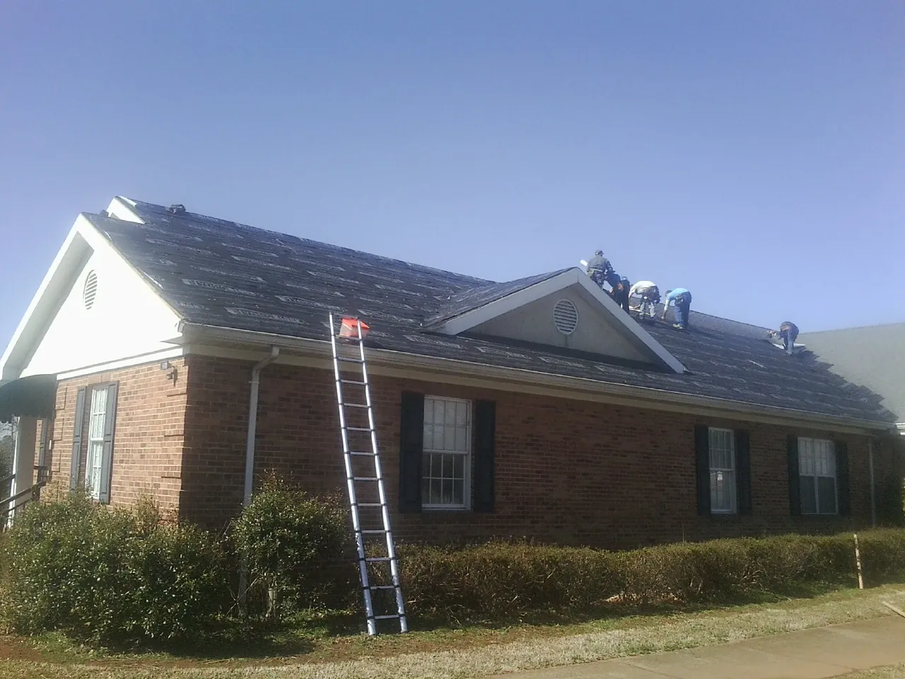 Crew tearing shingles off a brick ranch roof with a ladder set — Emergency Roof Repair work by our crew in Zellwood