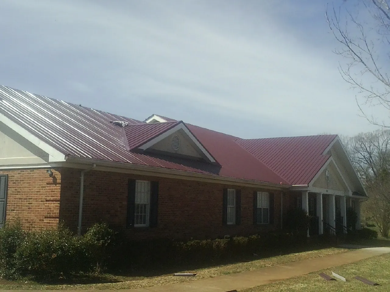 Red metal roof with gabled entries on a long brick building, from a Hail Damage Roof Repair job in Zellwood