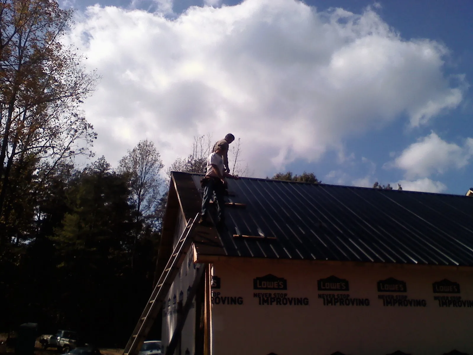 Roofer fastening dark metal panels high against a cloudy sky, from a Roof Inspection job in Zellwood
