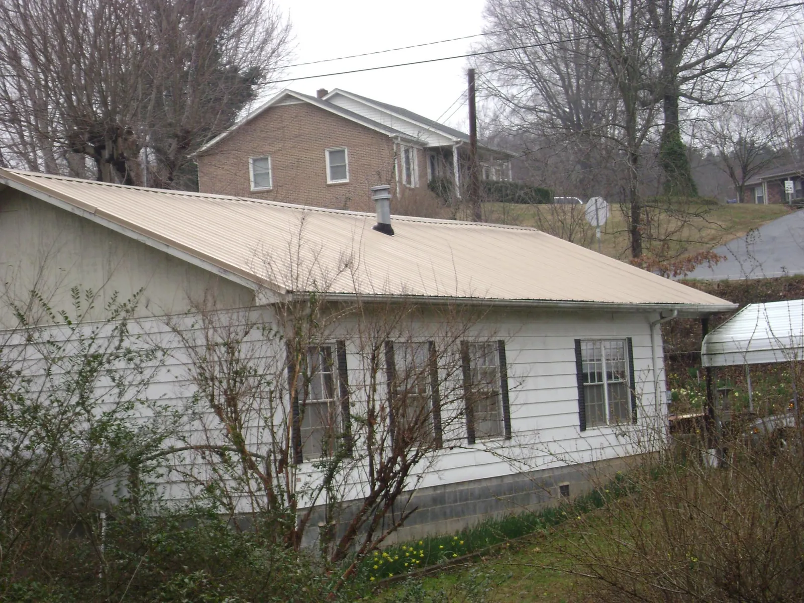 Tan metal roof on a white sided house set into a hillside — Commercial Roofing by Roofing Brothers in Zellwood